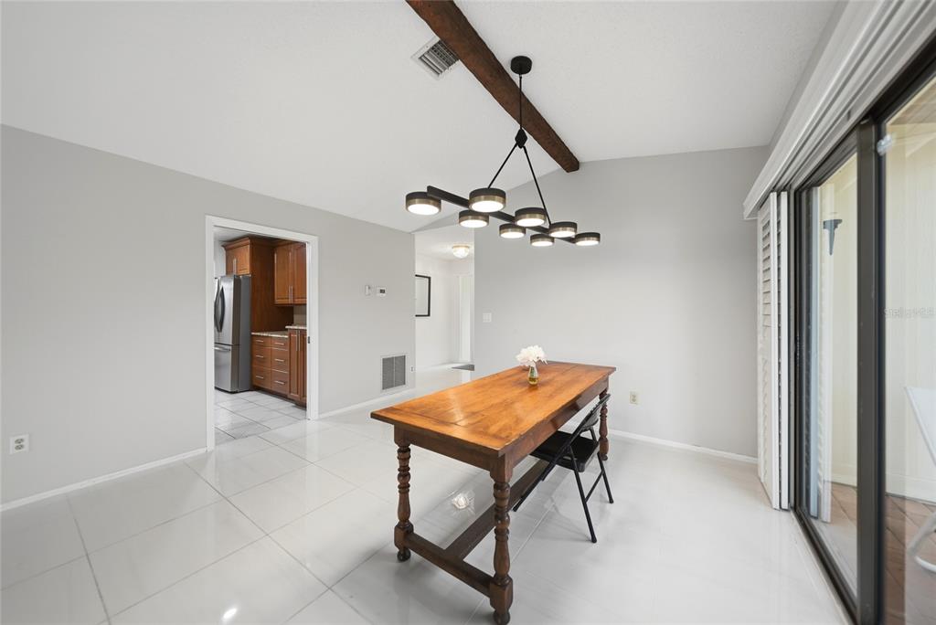 A dining room with white tile floors, a wooden table, and a modern chandelier — 49 SANDSTONE CIRCLE, VENICE, FL