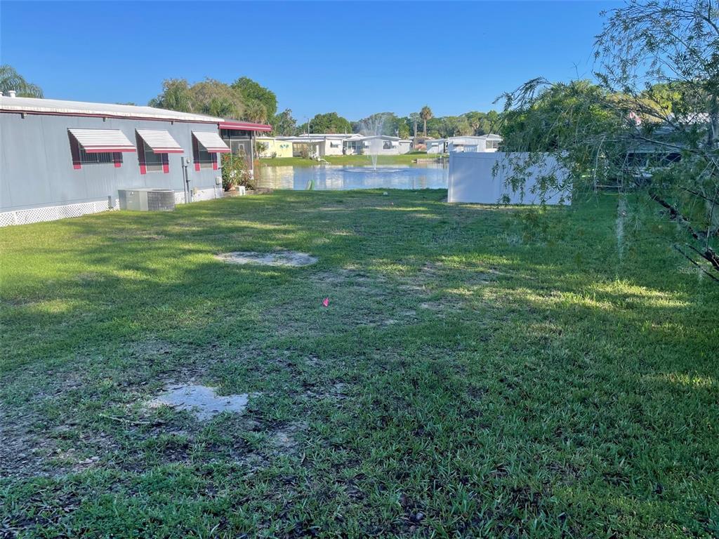 A grassy backyard leads to a small lake with a fountain behind a mobile home — 204 ALLYSON ROAD, LEESBURG, FL