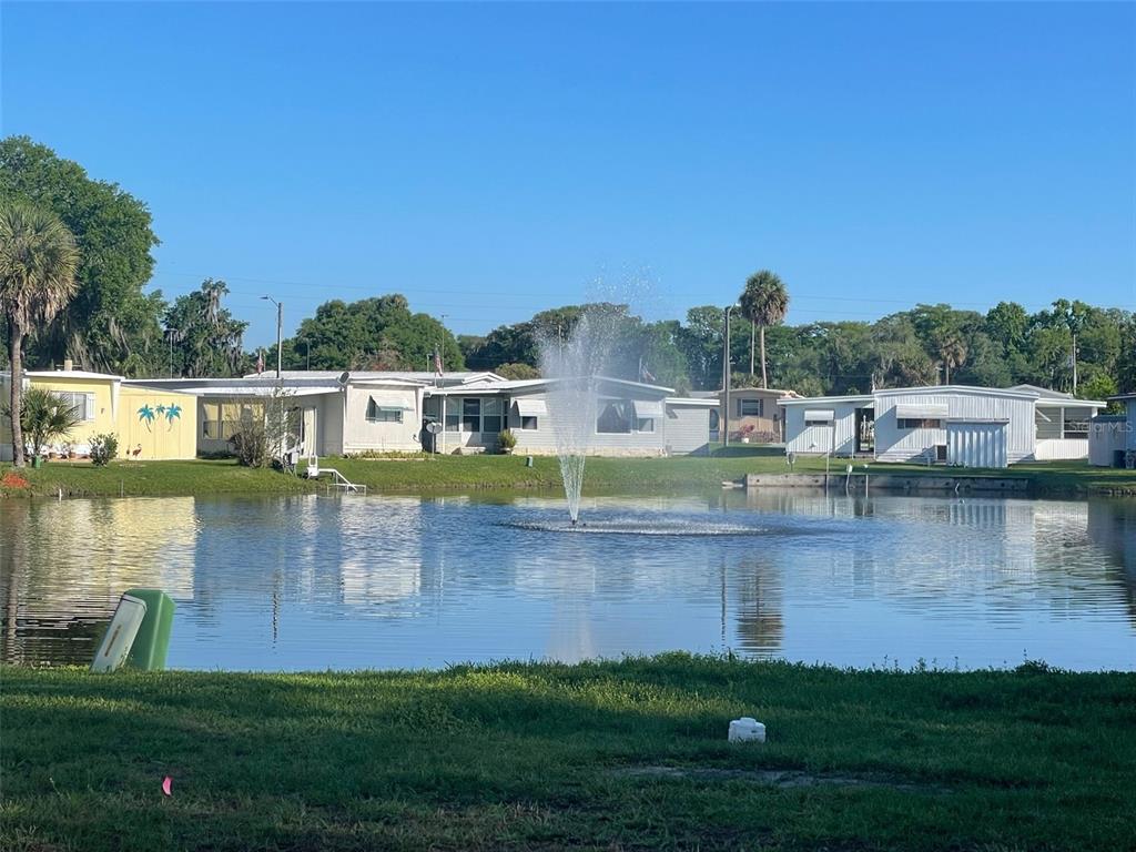 A pond with a fountain sits in front of several mobile homes under a clear sky — 204 ALLYSON ROAD, LEESBURG, FL