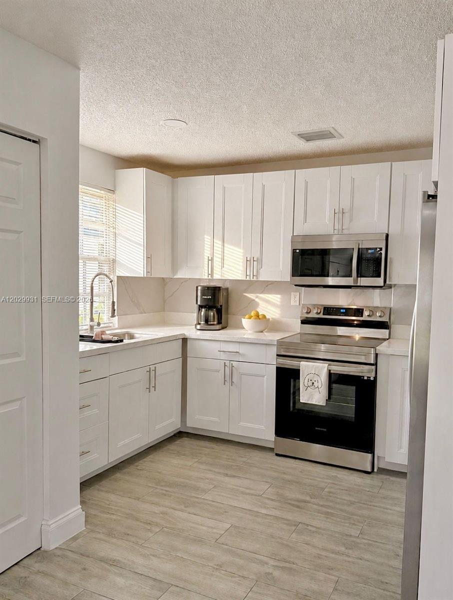 A kitchen features white shaker cabinets, stainless steel appliances, and light wood-look tile flooring — 5519 NW 4th Ave, Miami FL 33127, MIAMI, FL