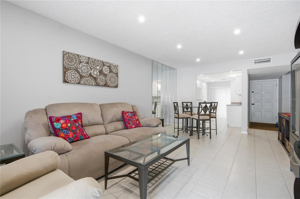 A living room with a beige sofa, glass coffee table, tile flooring, and dining area — 2052 SUNSET POINT ROAD UNIT 45, CLEARWATER, FL