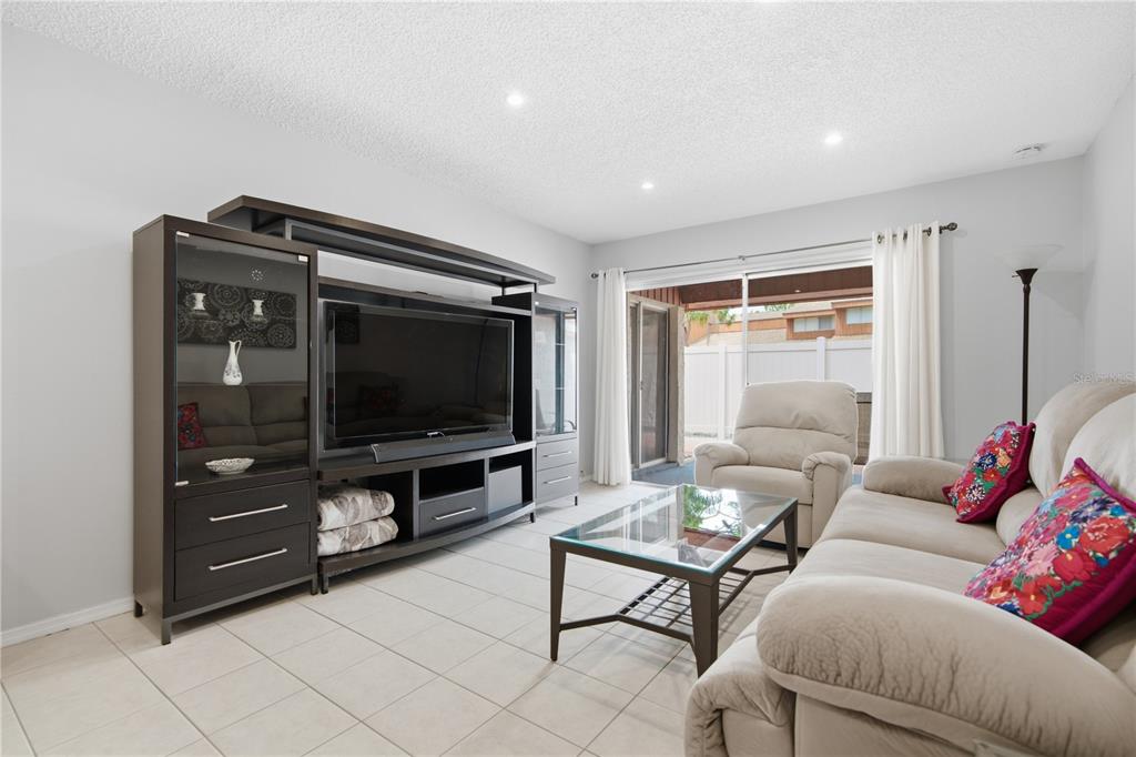 A living room features a large entertainment center, a glass coffee table, and beige furniture — 2052 SUNSET POINT ROAD UNIT 45, CLEARWATER, FL