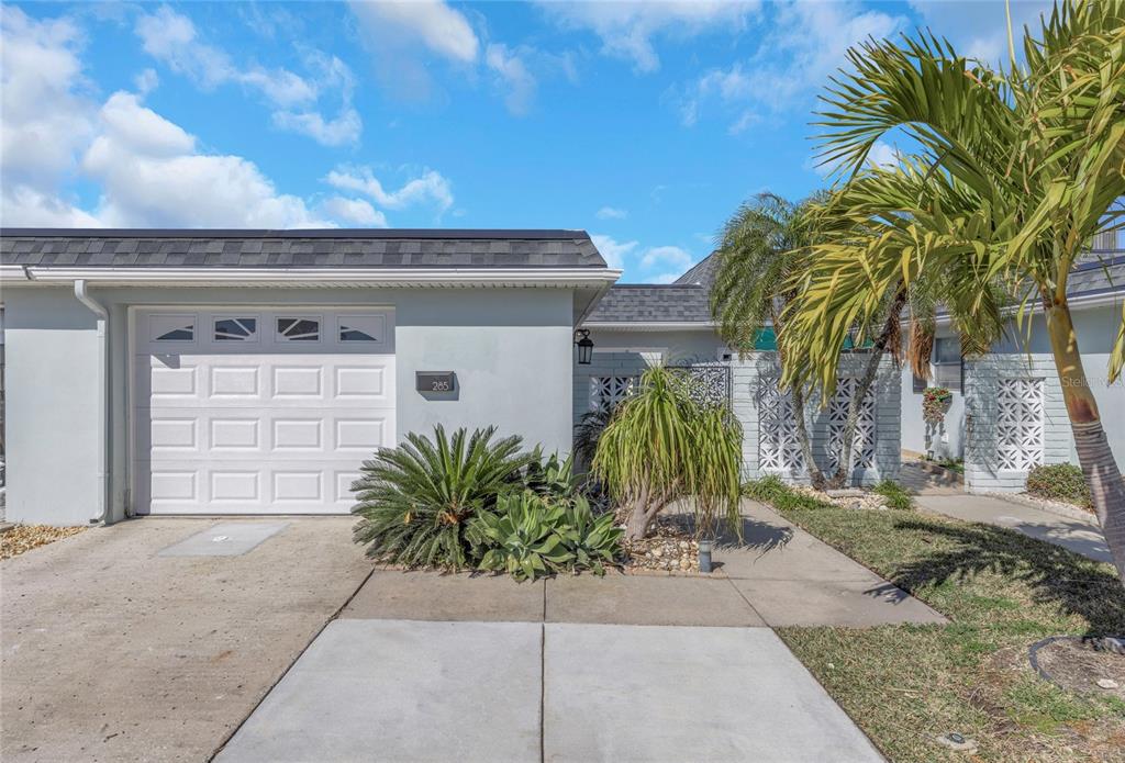 A light gray house exterior features a white garage door, concrete driveway, and tropical landscaping — 285 BOCA CIEGA POINT BOULEVARD N UNIT 3009, ST PETERSBURG, FL