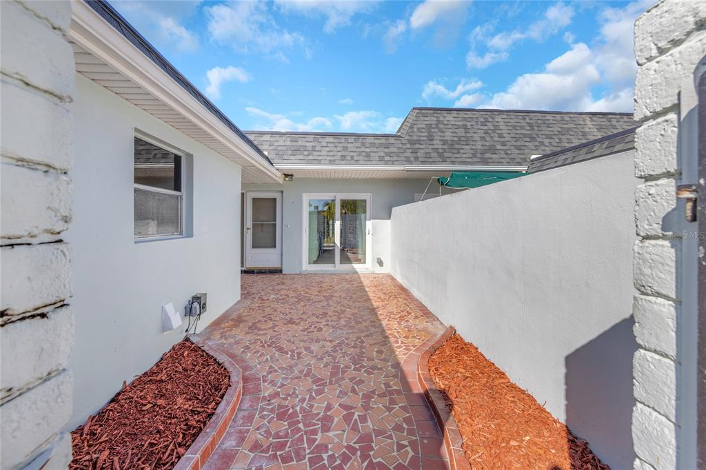 A paved courtyard with red mulch borders sits between a house exterior and a wall — 285 BOCA CIEGA POINT BOULEVARD N UNIT 3009, ST PETERSBURG, FL