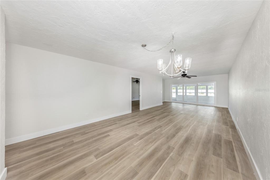 A spacious, empty room features light wood-look flooring, white walls, and a modern chandelier — 285 BOCA CIEGA POINT BOULEVARD N UNIT 3009, ST PETERSBURG, FL