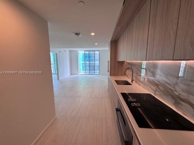 A modern kitchen with light wood cabinets and marble backsplash overlooks an open living area — 77 SE 5 ST # 1806, Miami FL 33131, MIAMI, FL