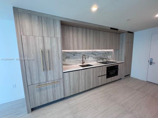 A modern kitchen features wood-grain cabinetry, a marble backsplash, and integrated stainless steel appliances — 77 SE 5 ST # 1806, Miami FL 33131, MIAMI, FL
