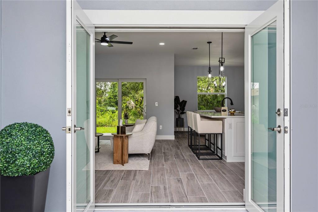 A view through open French doors into a living room and kitchen with tile floors — 2771 HALLADAY STREET, NORTH PORT, FL