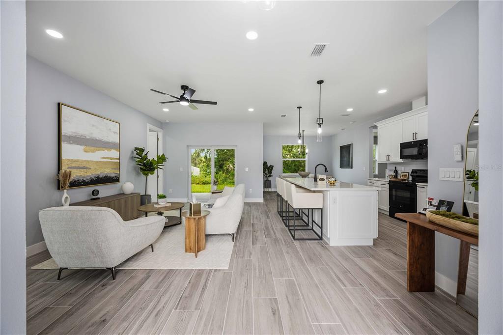 An open-concept living room and kitchen with white cabinets, a large island, and wood-look flooring — 2771 HALLADAY STREET, NORTH PORT, FL