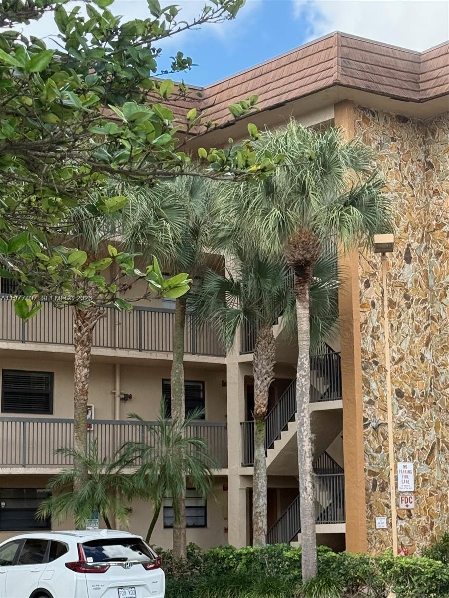 A multi-story apartment building exterior features stone siding, balconies, and several palm trees — 4940 E Sabal Palm Blvd # 203, Tamarac FL 33319, TAMARAC, FL
