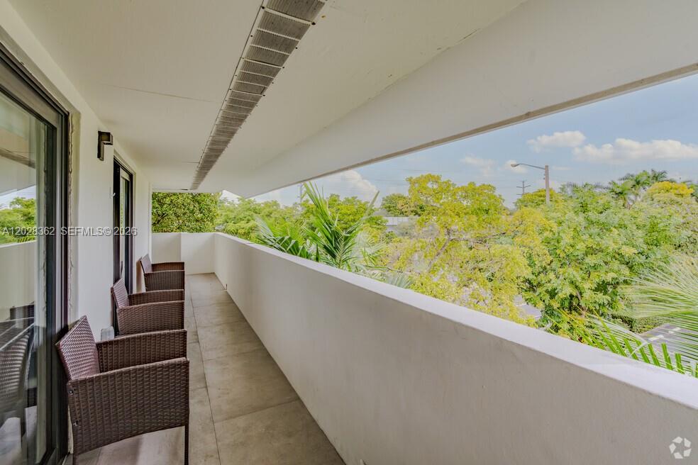 A balcony with tiled flooring, wicker chairs, and a view of surrounding trees — 800 S Dixie Hwy 203 Hwy # 203, Coral Gables FL 33146, CORAL GABLES, FL