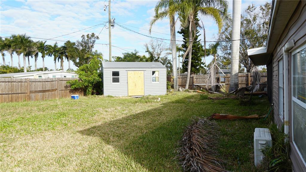 A backyard features a gray storage shed, a wooden fence, palm trees, and grass — 3513 ARECA STREET, PUNTA GORDA, FL