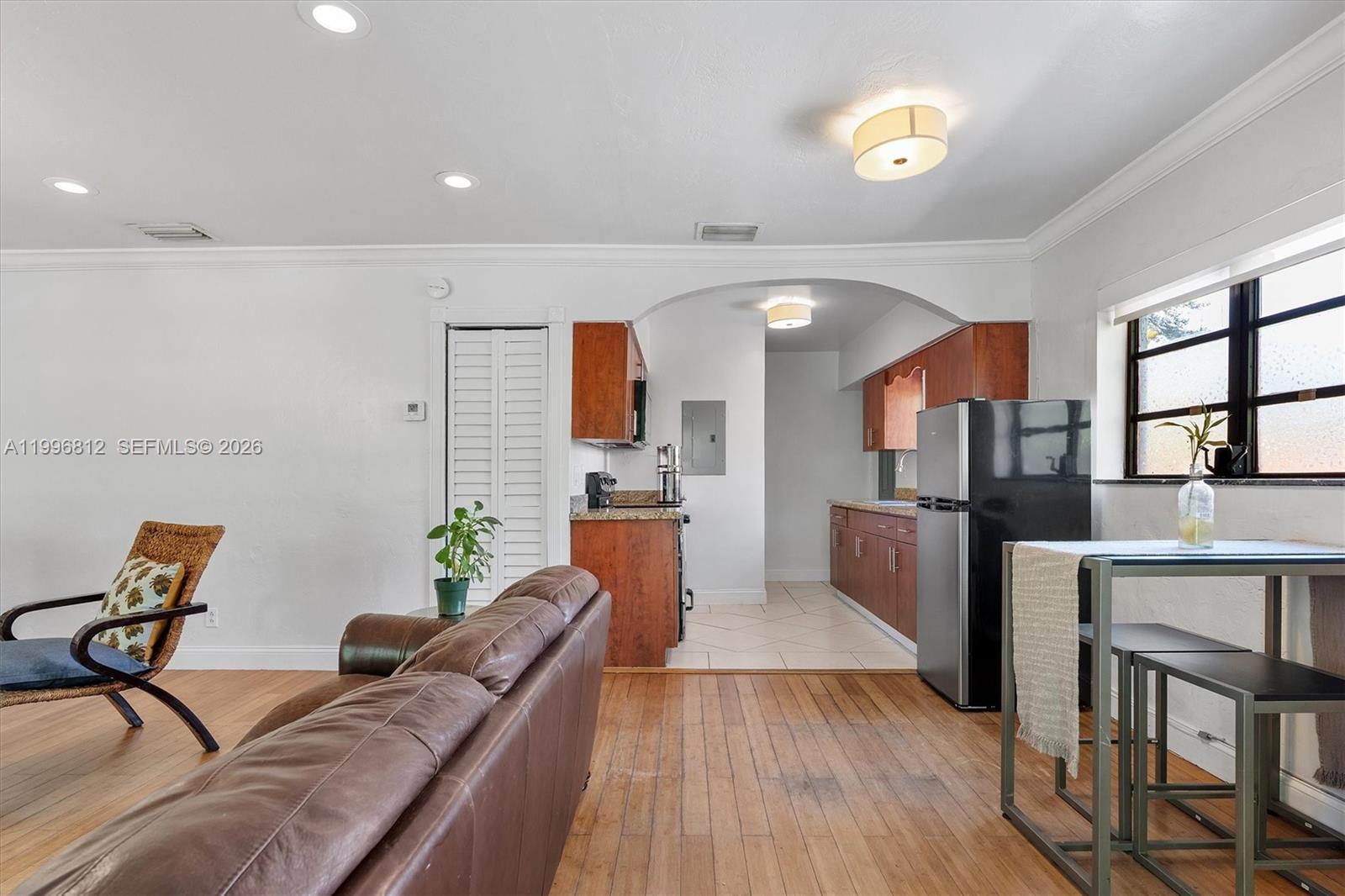 A living room with wood floors opens into a kitchen featuring wood cabinetry and tile — 1440 NE 148th St, Miami FL 33161, MIAMI, FL