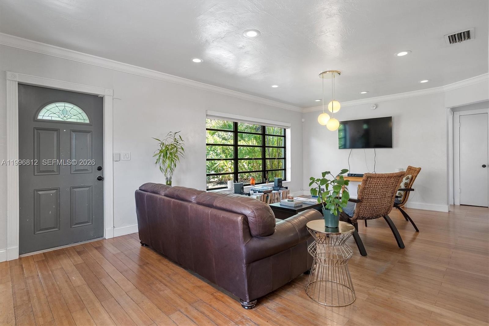 A living room features a brown leather sofa, wicker chairs, and a wall-mounted television — 1440 NE 148th St, Miami FL 33161, MIAMI, FL