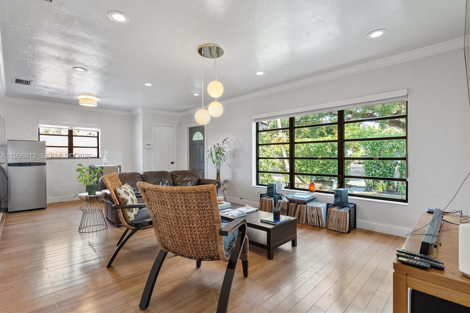 A living room features hardwood floors, a large window, and a modern globe pendant light — 1440 NE 148th St, Miami FL 33161, MIAMI, FL