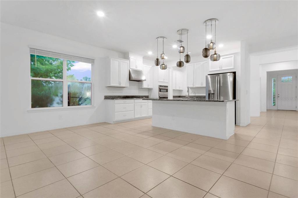 A kitchen features white cabinetry, granite countertops, a center island, and tile flooring — 901 SABAL BREEZE LANE, APOPKA, FL