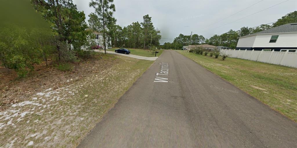 A paved residential street leads toward houses surrounded by trees and a white fence — 2065 W TACOMA DRIVE, CITRUS SPRINGS, FL