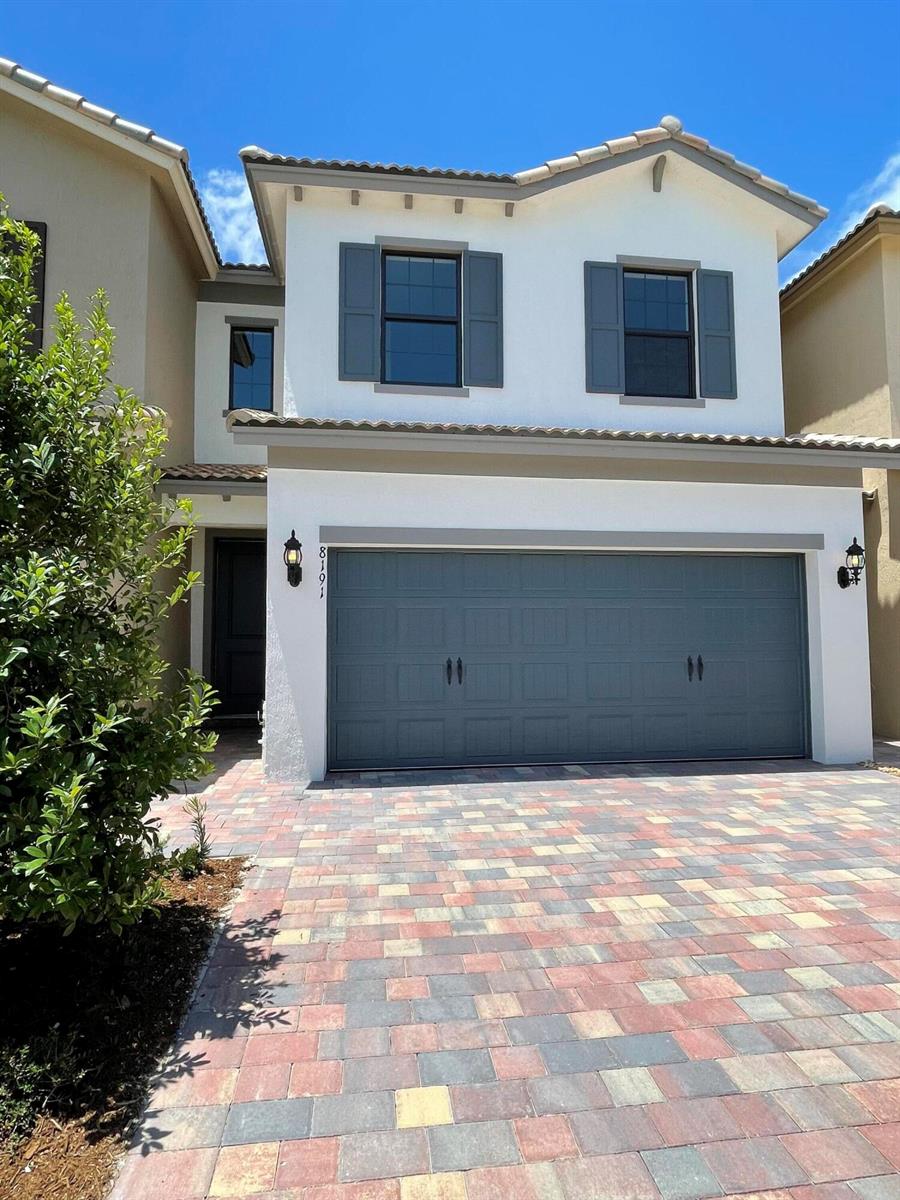 A two-story house with a white stucco exterior, gray garage door, and paver driveway — 8191 Cinch Way, Lake Worth FL 33467, LAKE WORTH, FL