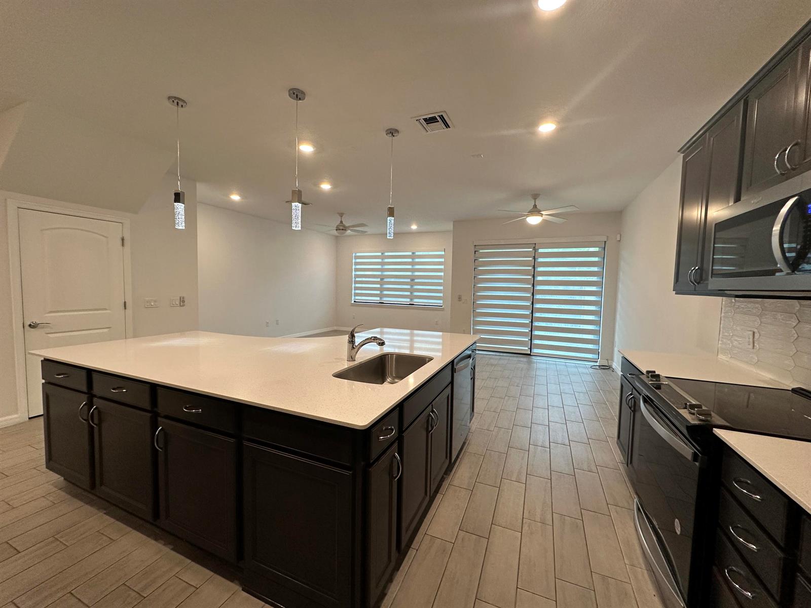 A modern kitchen features a large island with a sink, dark cabinets, and tile flooring — 8191 Cinch Way, Lake Worth FL 33467, LAKE WORTH, FL