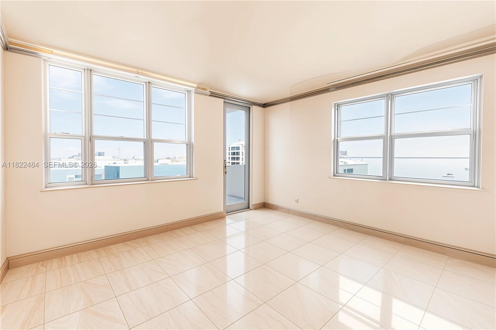 An empty room features light-colored tile flooring, beige walls, and large windows with water views — 100 Lincoln Rd # 811, Miami Beach FL 33139, MIAMI BEACH, FL