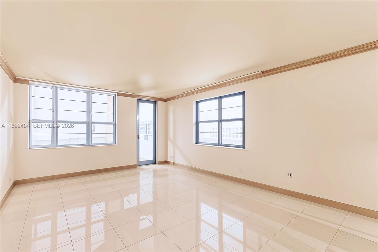An empty room features light-colored tile flooring, beige walls, crown molding, and large windows — 100 Lincoln Rd # 811, Miami Beach FL 33139, MIAMI BEACH, FL