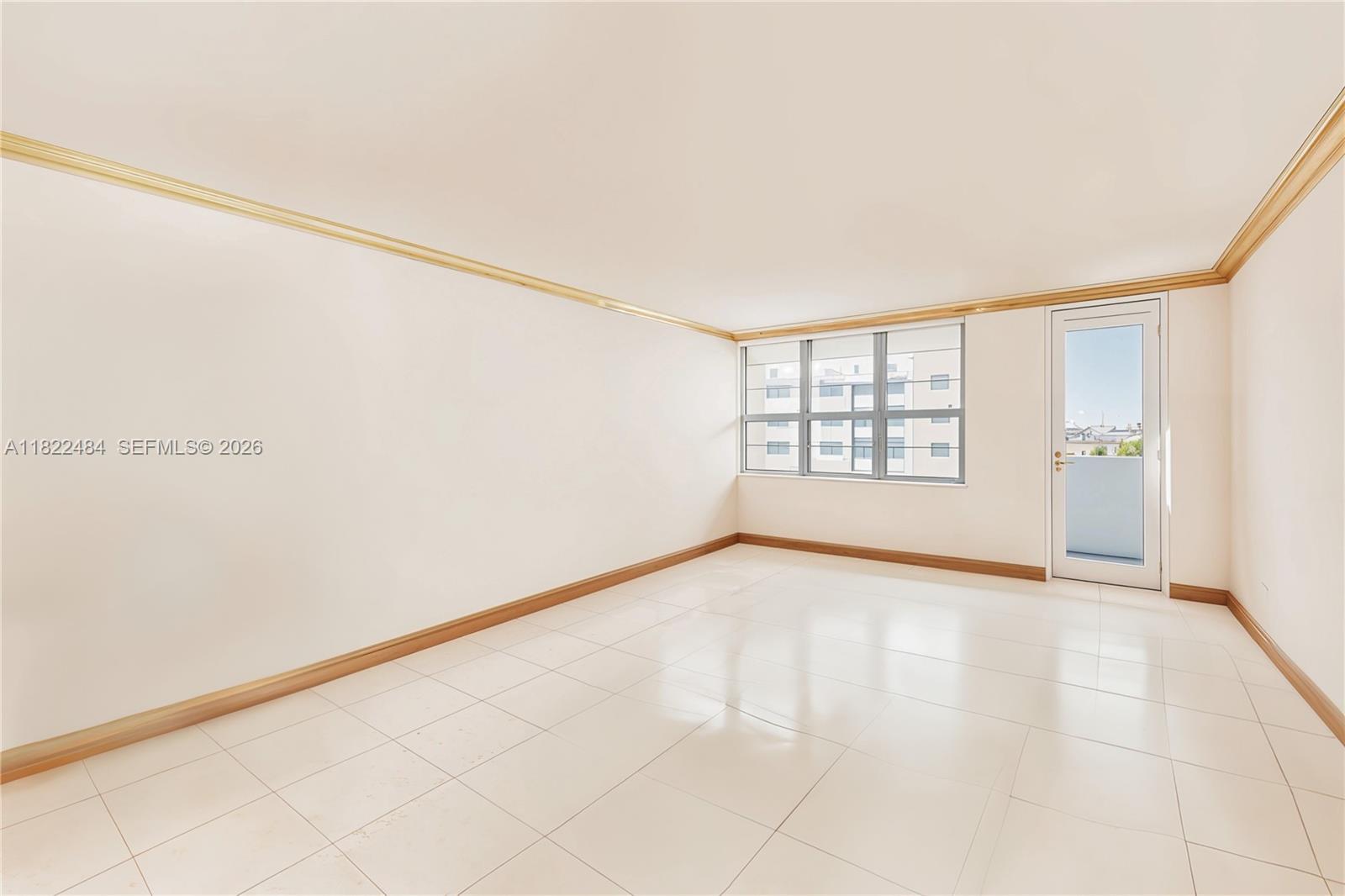 An empty room features white tile flooring, beige walls, crown molding, and a glass balcony door — 100 Lincoln Rd # 811, Miami Beach FL 33139, MIAMI BEACH, FL