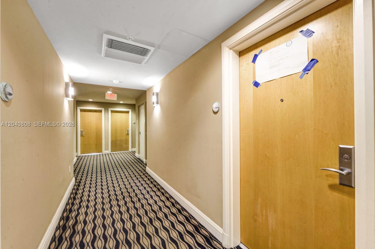 A hallway with patterned carpet leads to several wooden doors under recessed lighting — 244 Biscayne Blvd # 2005, Miami FL 33132, MIAMI, FL