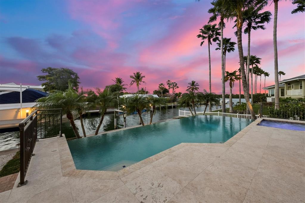 An infinity pool and spa overlook a canal at sunset with palm trees nearby — 761 NORTON STREET, LONGBOAT KEY, FL