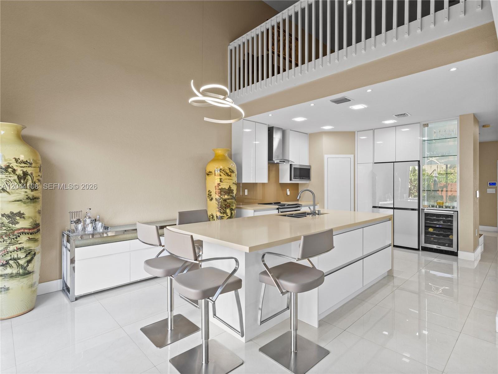 A modern kitchen features a large island with bar stools, white cabinetry, and tile flooring — 7086 NW 116th Ct, Doral FL 33178, DORAL, FL