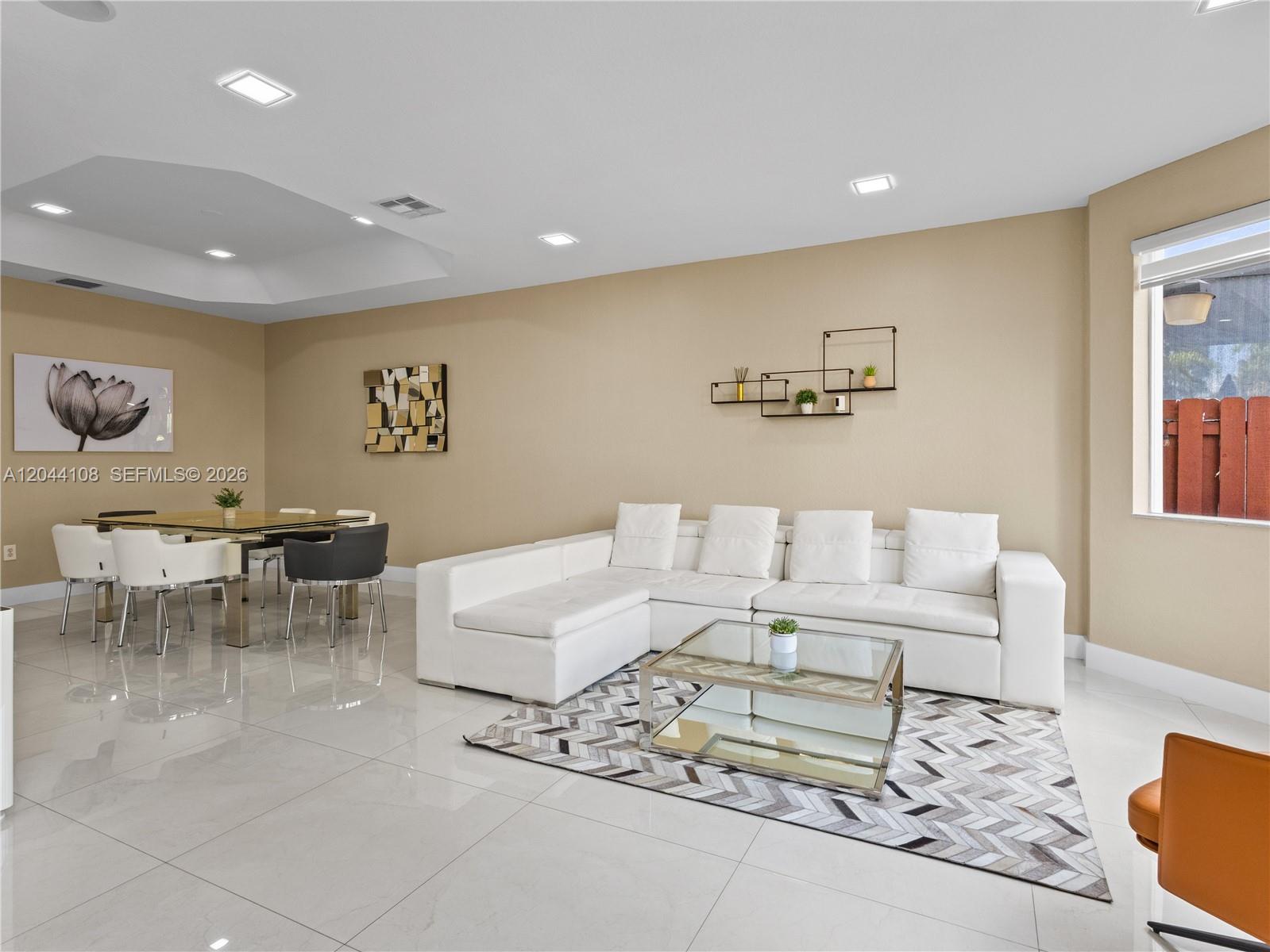 A living and dining area features white tile floors, a white sectional sofa, and neutral walls — 7086 NW 116th Ct, Doral FL 33178, DORAL, FL