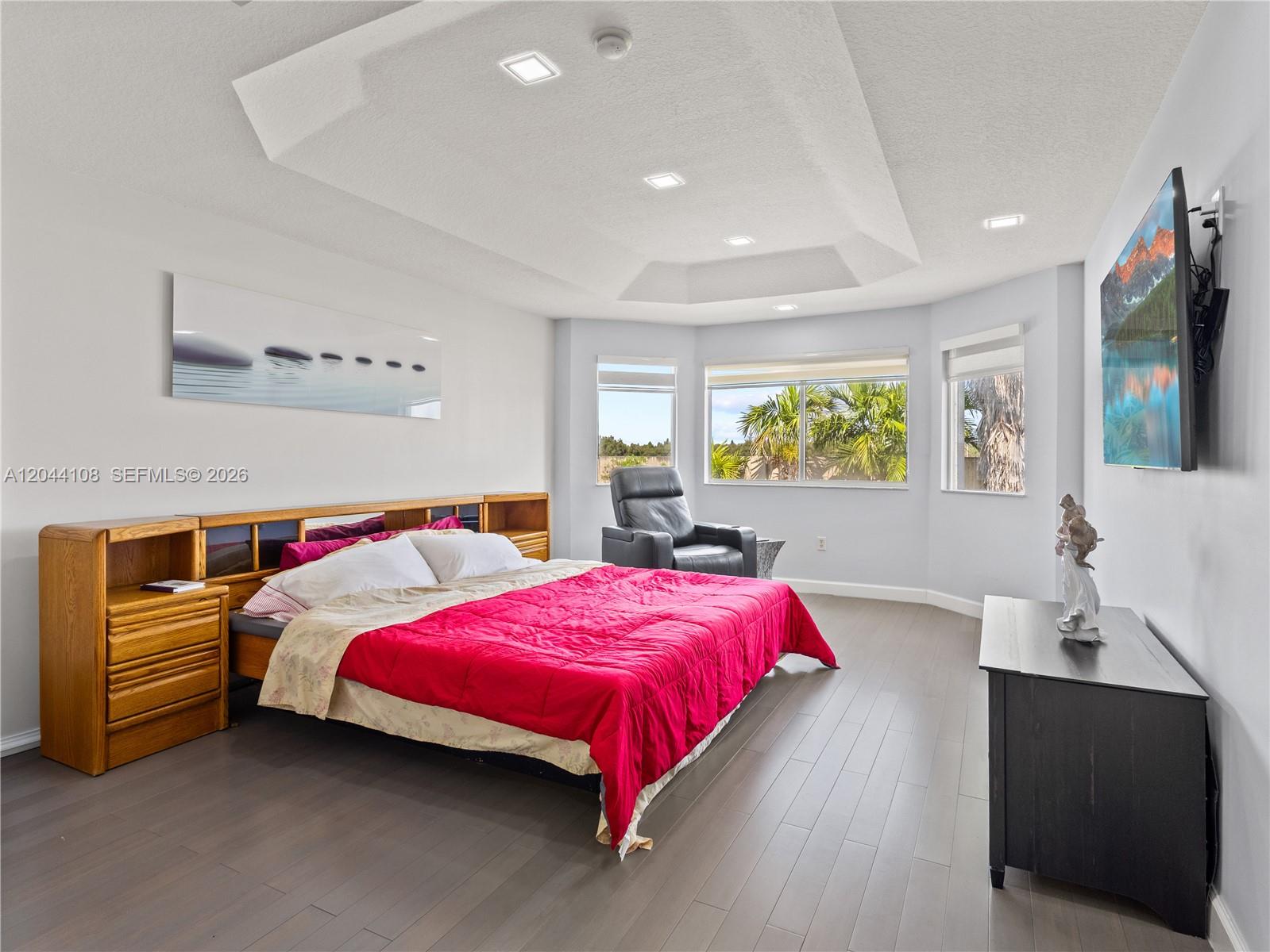 A bedroom features a tray ceiling, wood-toned headboard, red bedding, and a wall-mounted television — 7086 NW 116th Ct, Doral FL 33178, DORAL, FL
