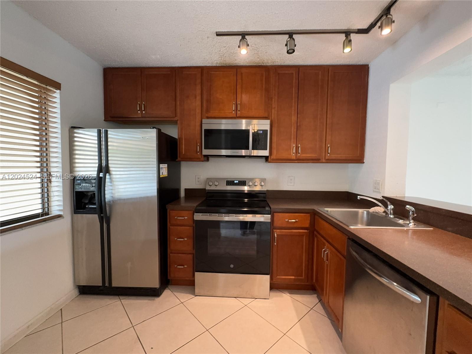 A kitchen features wood cabinets, stainless steel appliances, dark countertops, and tile flooring — 6552 Arleigh Ct # 102, Boca Raton FL 33433, BOCA RATON, FL