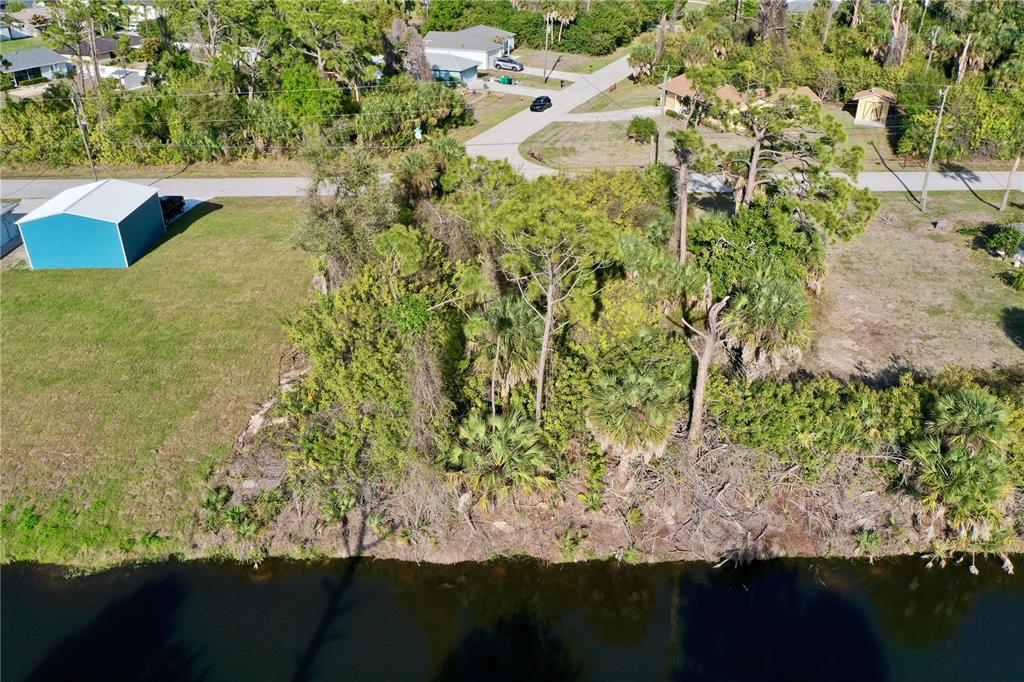 An aerial view shows a wooded, undeveloped residential lot bordering a canal — 7241 JENNIFER DRIVE, PORT CHARLOTTE, FL
