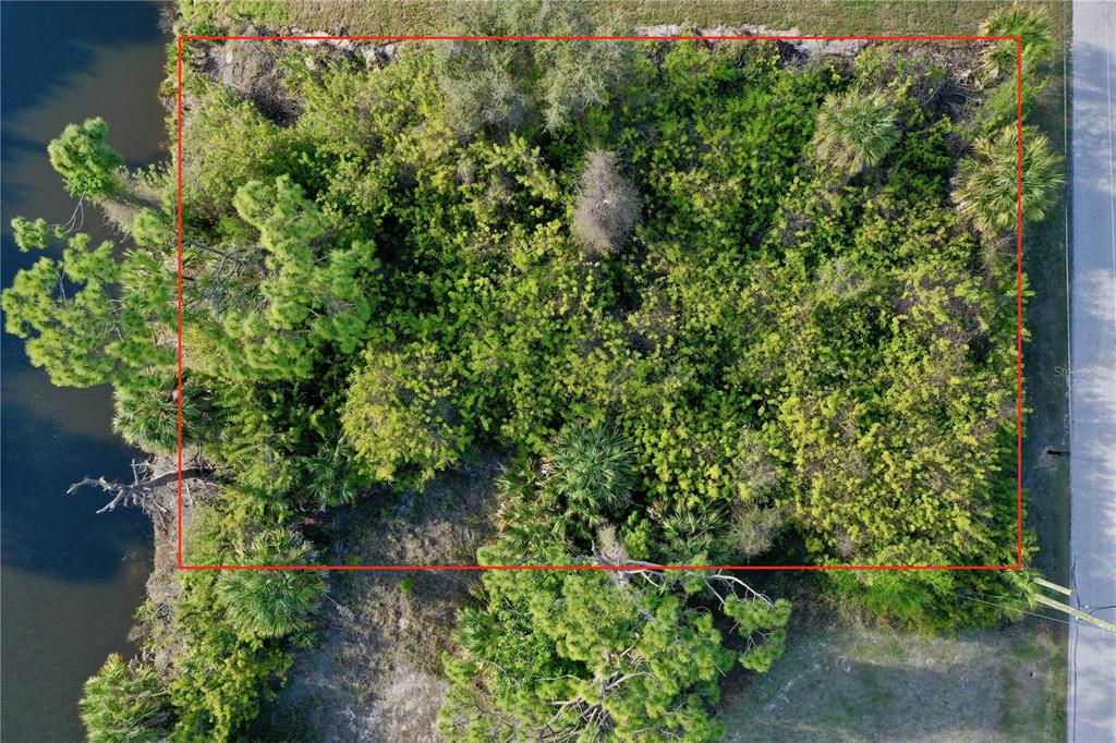 An aerial view shows a rectangular, heavily wooded vacant lot bordering a body of water — 7241 JENNIFER DRIVE, PORT CHARLOTTE, FL