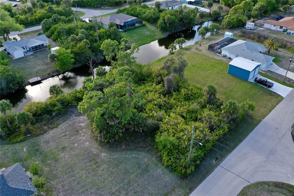An aerial view shows a vacant, wooded residential lot situated along a canal — 7241 JENNIFER DRIVE, PORT CHARLOTTE, FL