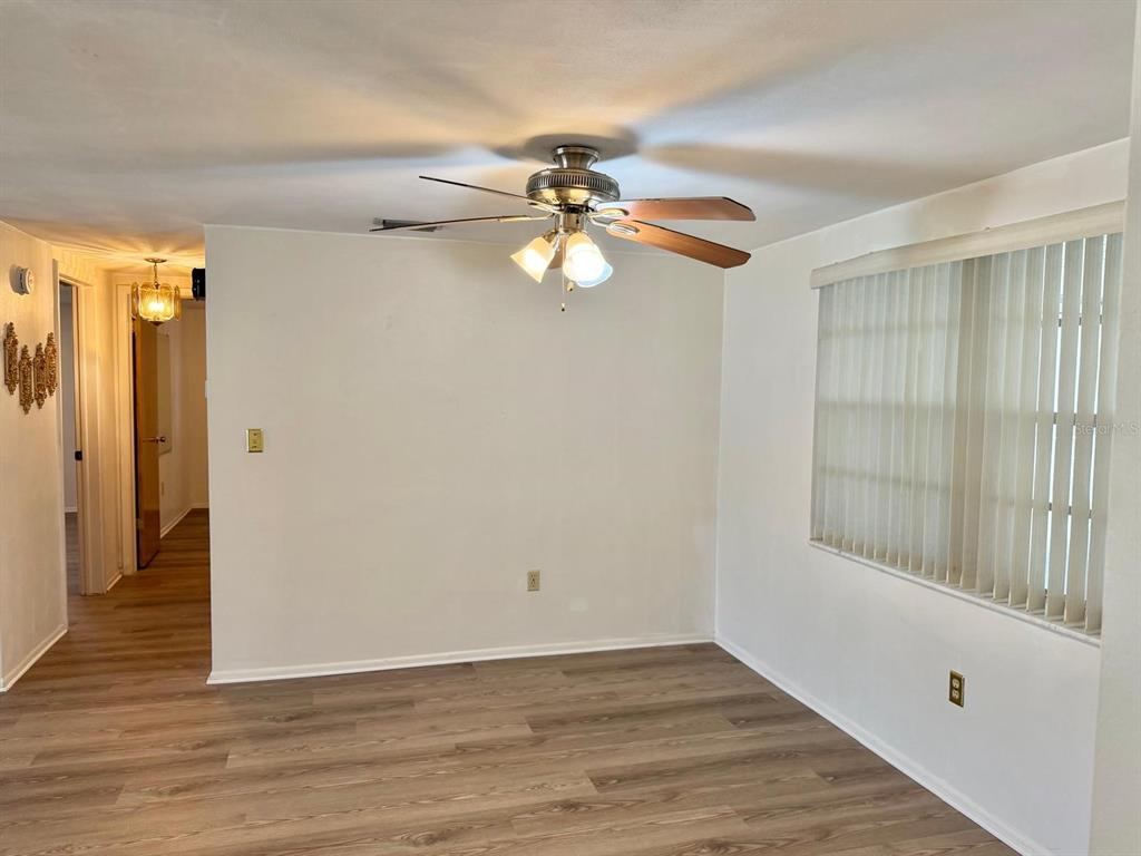 An empty room features wood-look flooring, a ceiling fan with lights, and vertical window blinds — 7434 NEVA LANE, PORT RICHEY, FL