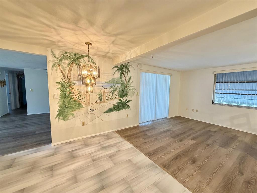 A living room features a palm tree mural, a tiered chandelier, and wood-look flooring — 7434 NEVA LANE, PORT RICHEY, FL