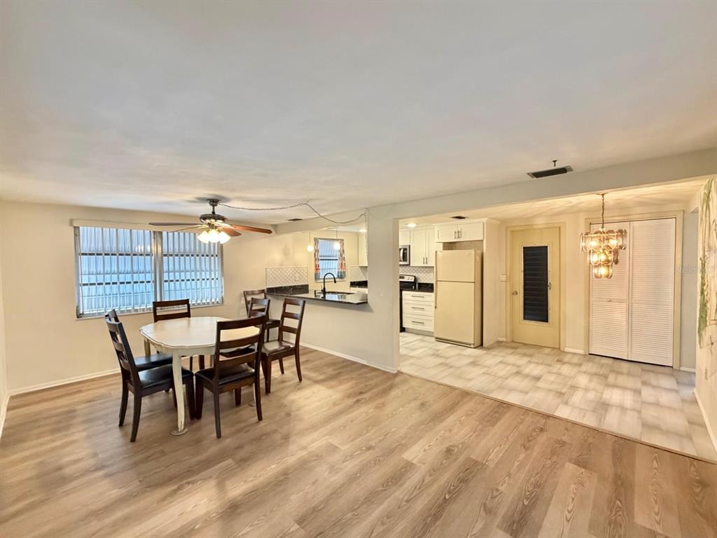 A dining area with wood-look flooring transitions into a kitchen with white cabinets and tile — 7434 NEVA LANE, PORT RICHEY, FL