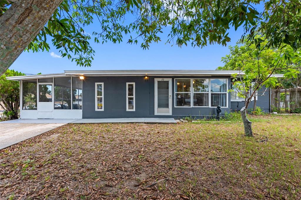 A single-story gray house features a screened-in porch, a concrete driveway, and a grassy yard — 72 LAKE SHORE DRIVE, PALM HARBOR, FL