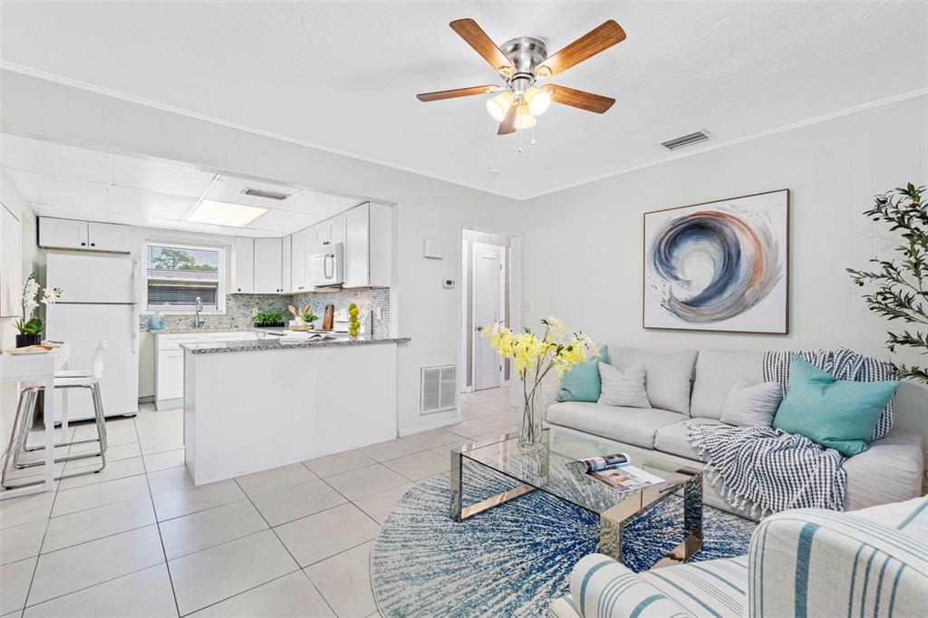 A sunroom with a glass-topped dining table, wicker chairs, and a view into a kitchen — 72 LAKE SHORE DRIVE, PALM HARBOR, FL