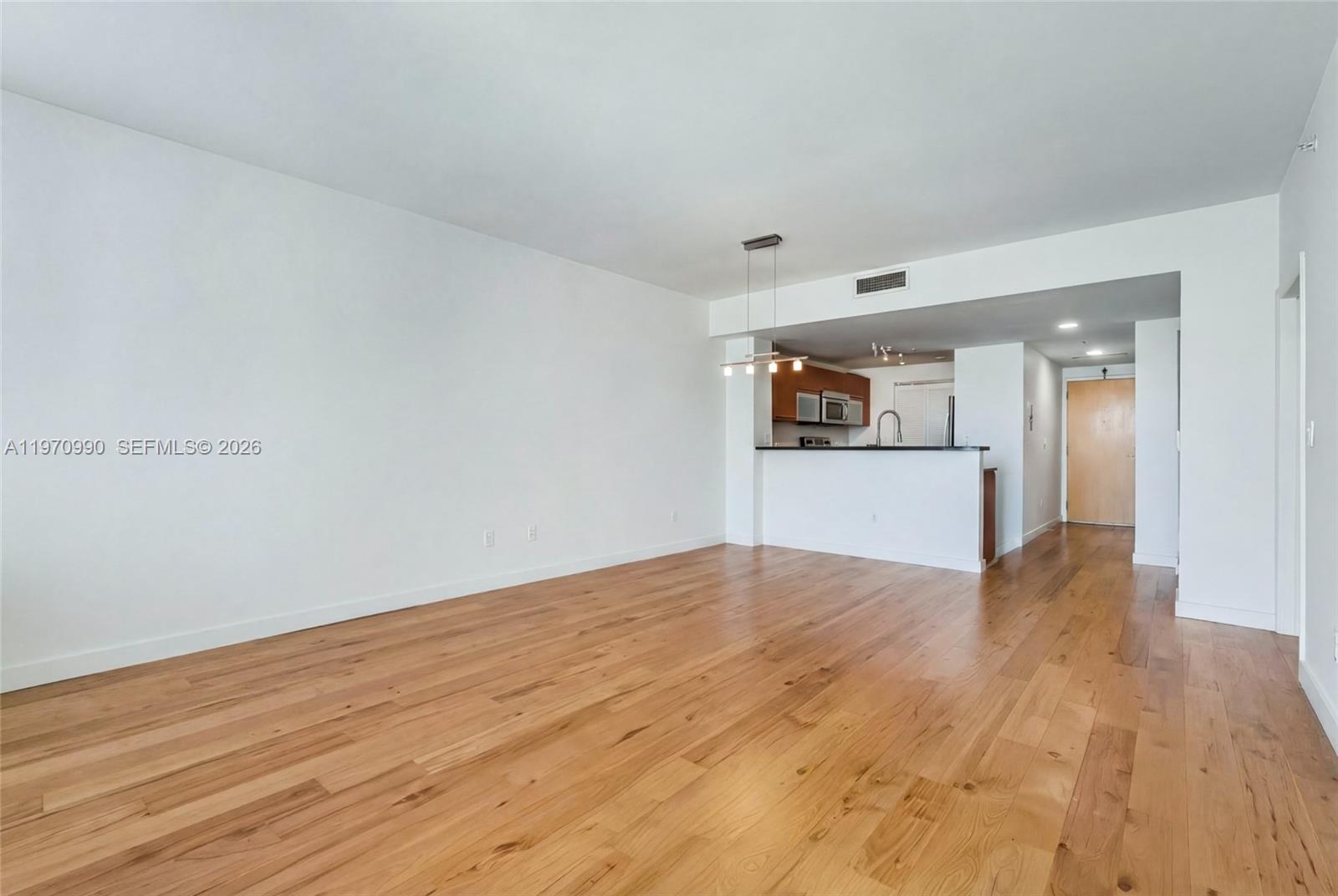 An empty living room features hardwood floors, white walls, and an open kitchen with a breakfast bar — 253 NE 2nd St # 1007, Miami FL 33132, MIAMI, FL