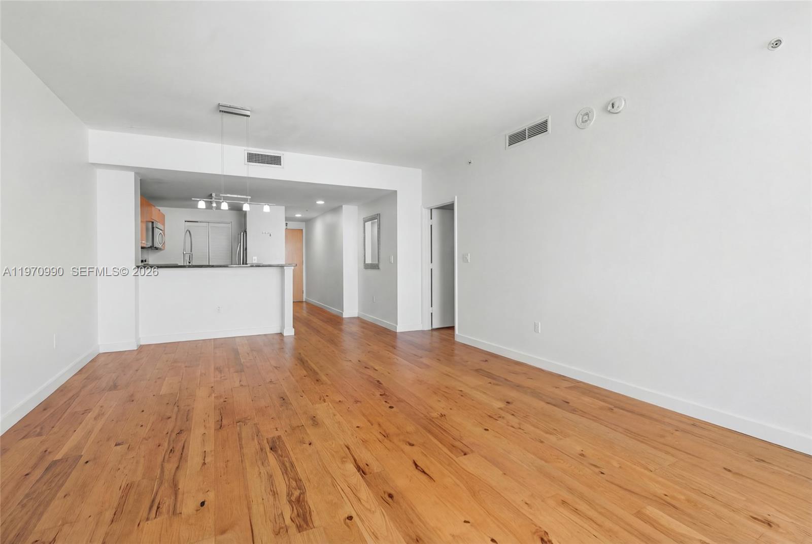 An unfurnished living area features hardwood flooring, white walls, and an open kitchen with cabinetry — 253 NE 2nd St # 1007, Miami FL 33132, MIAMI, FL
