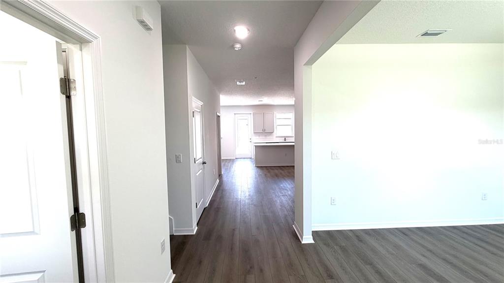 A hallway with wood-look flooring leads from a foreground room toward a kitchen area — 706 BLISSFUL GARDENS WAY, APOPKA, FL