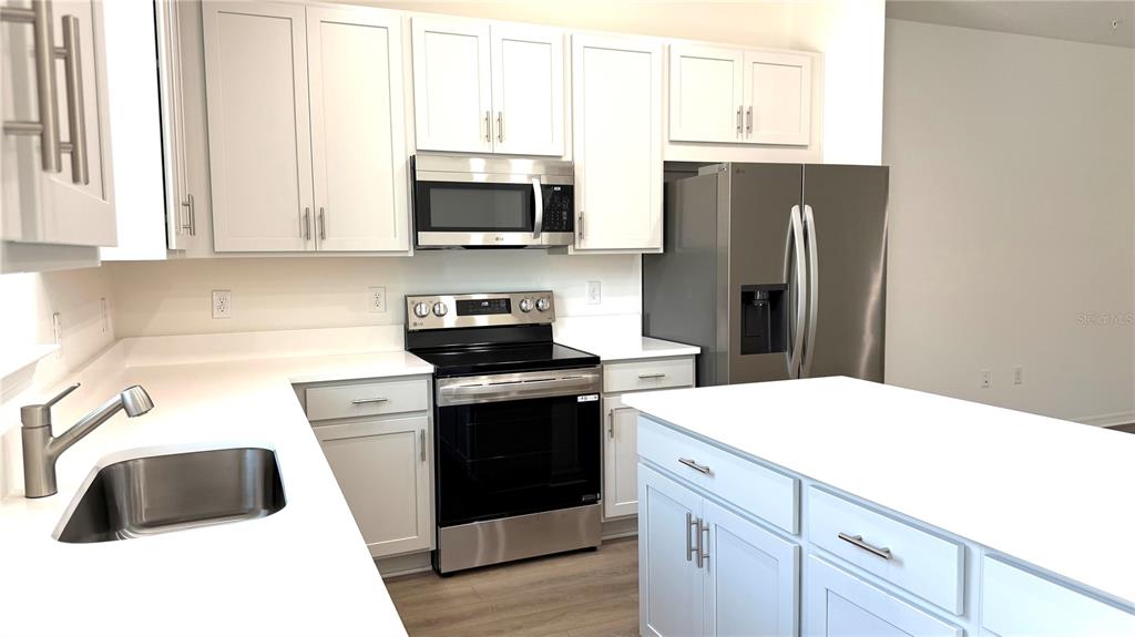 A kitchen with white cabinets, stainless steel appliances, and a central island with white countertops — 706 BLISSFUL GARDENS WAY, APOPKA, FL
