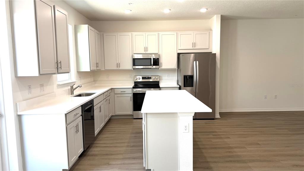 A modern kitchen features white cabinets, stainless steel appliances, a center island, and wood-look flooring — 706 BLISSFUL GARDENS WAY, APOPKA, FL