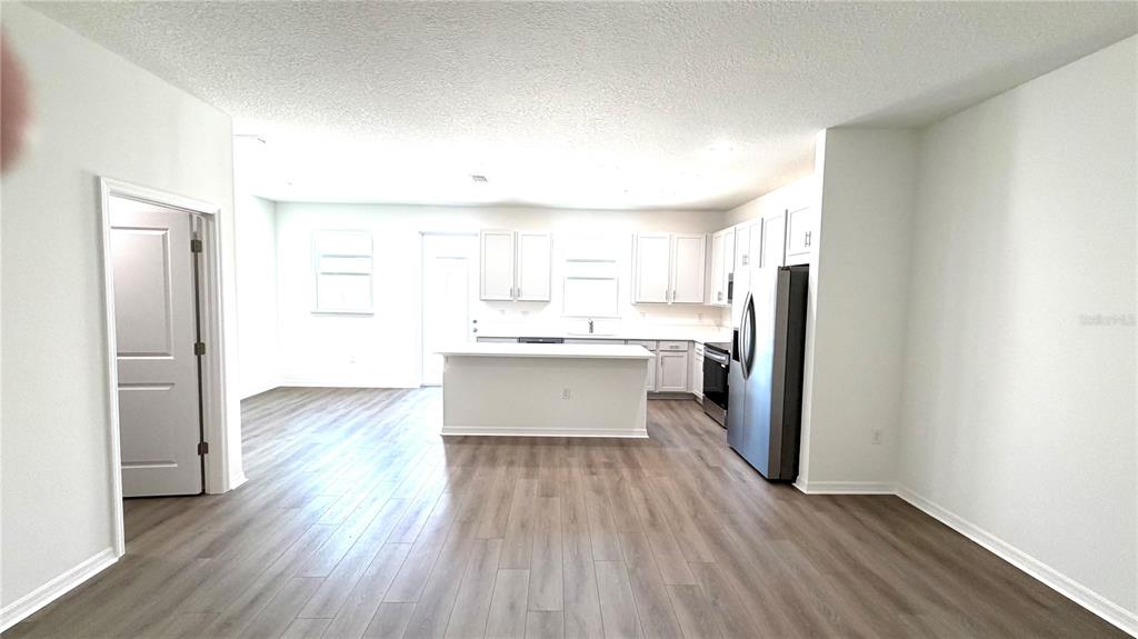 A kitchen features white cabinetry, a center island, stainless steel appliances, and wood-look flooring — 706 BLISSFUL GARDENS WAY, APOPKA, FL