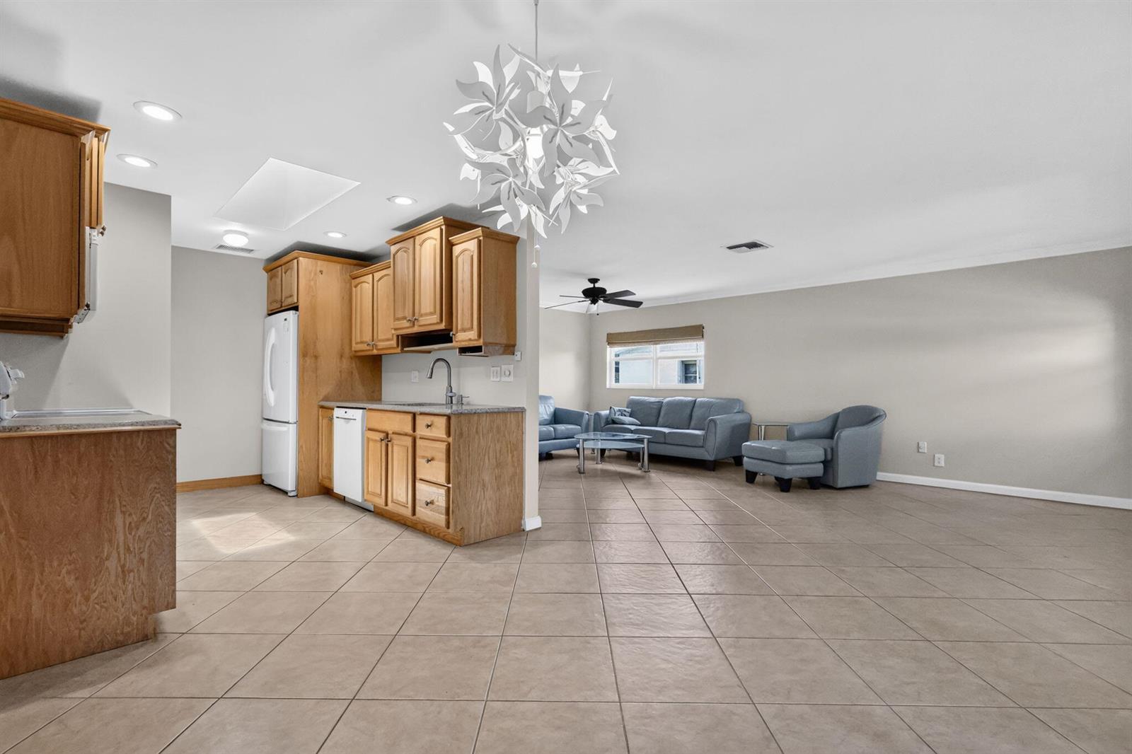 An open-concept kitchen with wood cabinets and tile floors flows into a living area — 3358 Christopher Street, West Palm Beach FL 33417, WEST PALM BEACH, FL