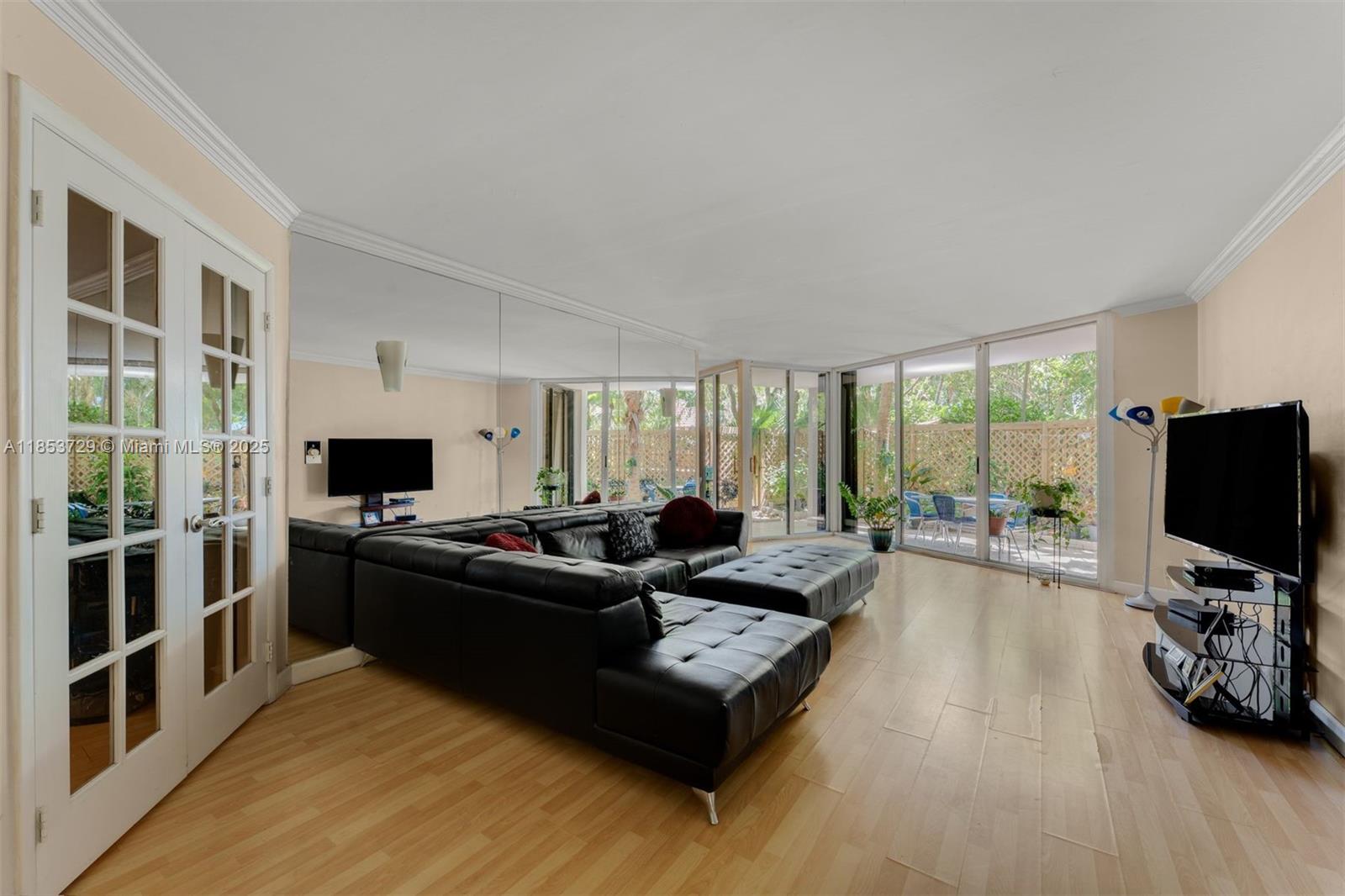 A living room features a large black sectional sofa, mirrored walls, and sliding glass doors — 2000 Towerside Ter # 308, Miami FL 33138, MIAMI, FL