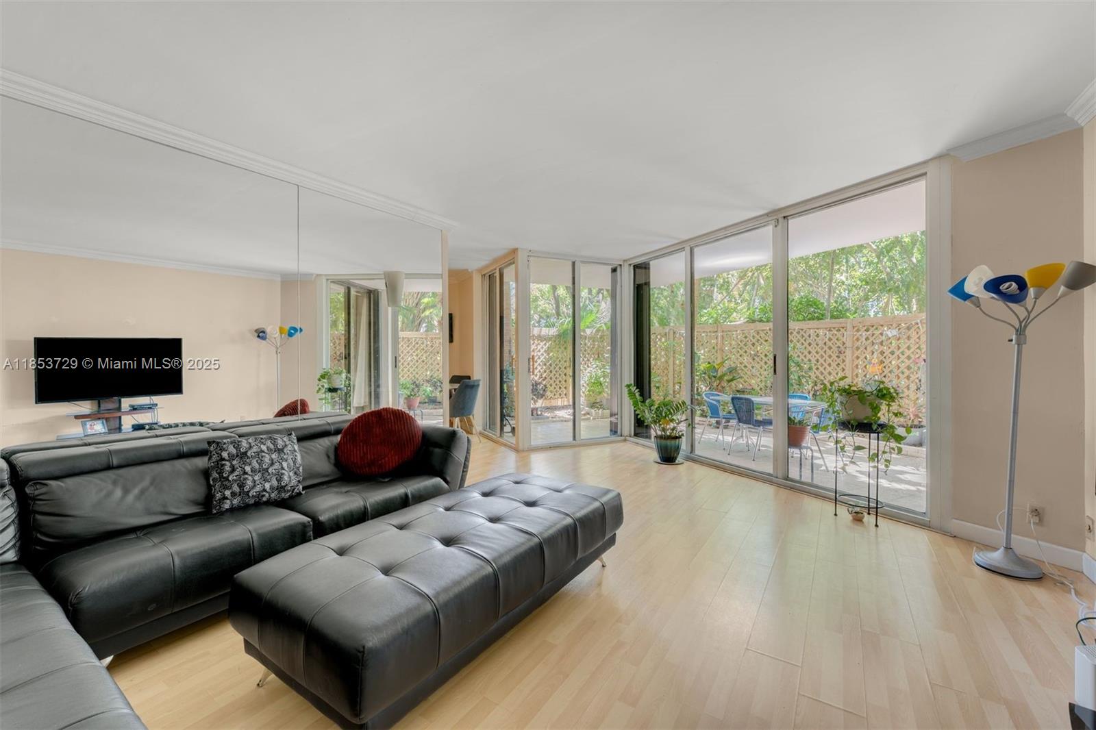 A living room with a black leather sofa, mirrored wall, and sliding doors to a patio — 2000 Towerside Ter # 308, Miami FL 33138, MIAMI, FL