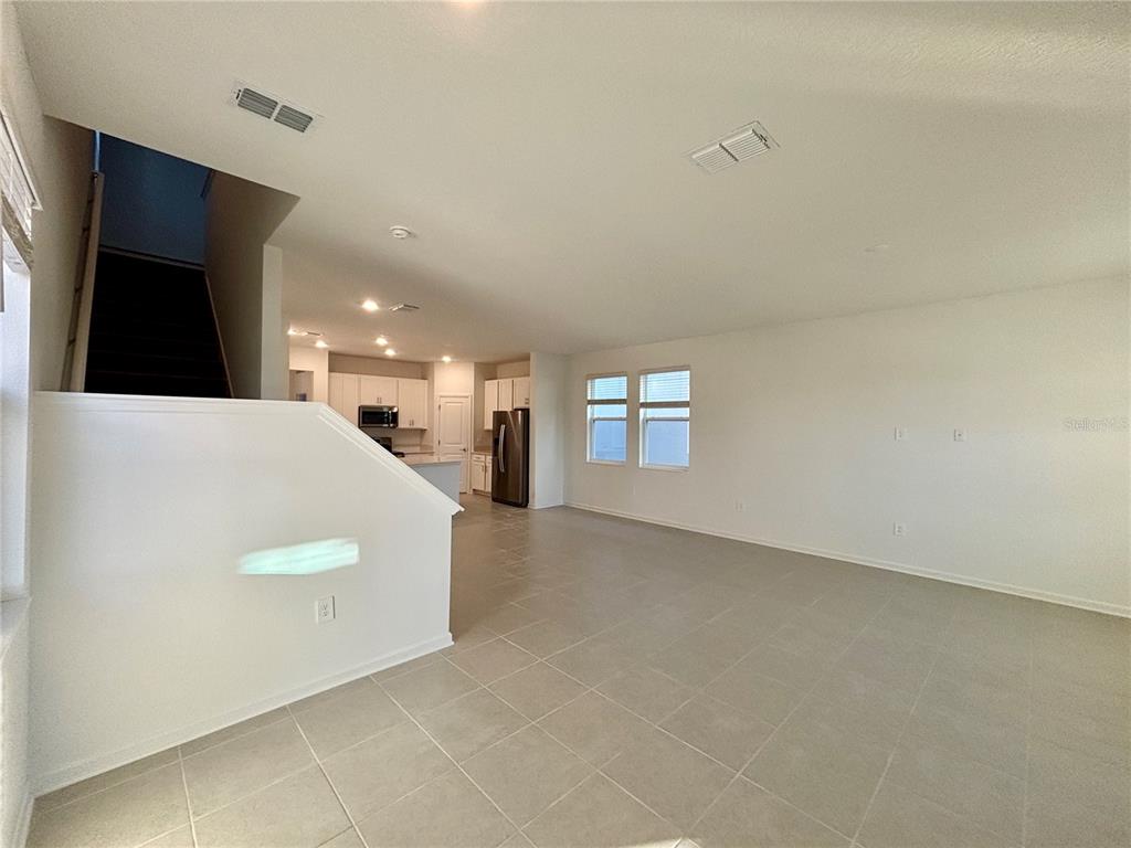 An open-concept living area with tile flooring, white walls, and a staircase leading upstairs — 5770 MEDITATION DRIVE, CLERMONT, FL